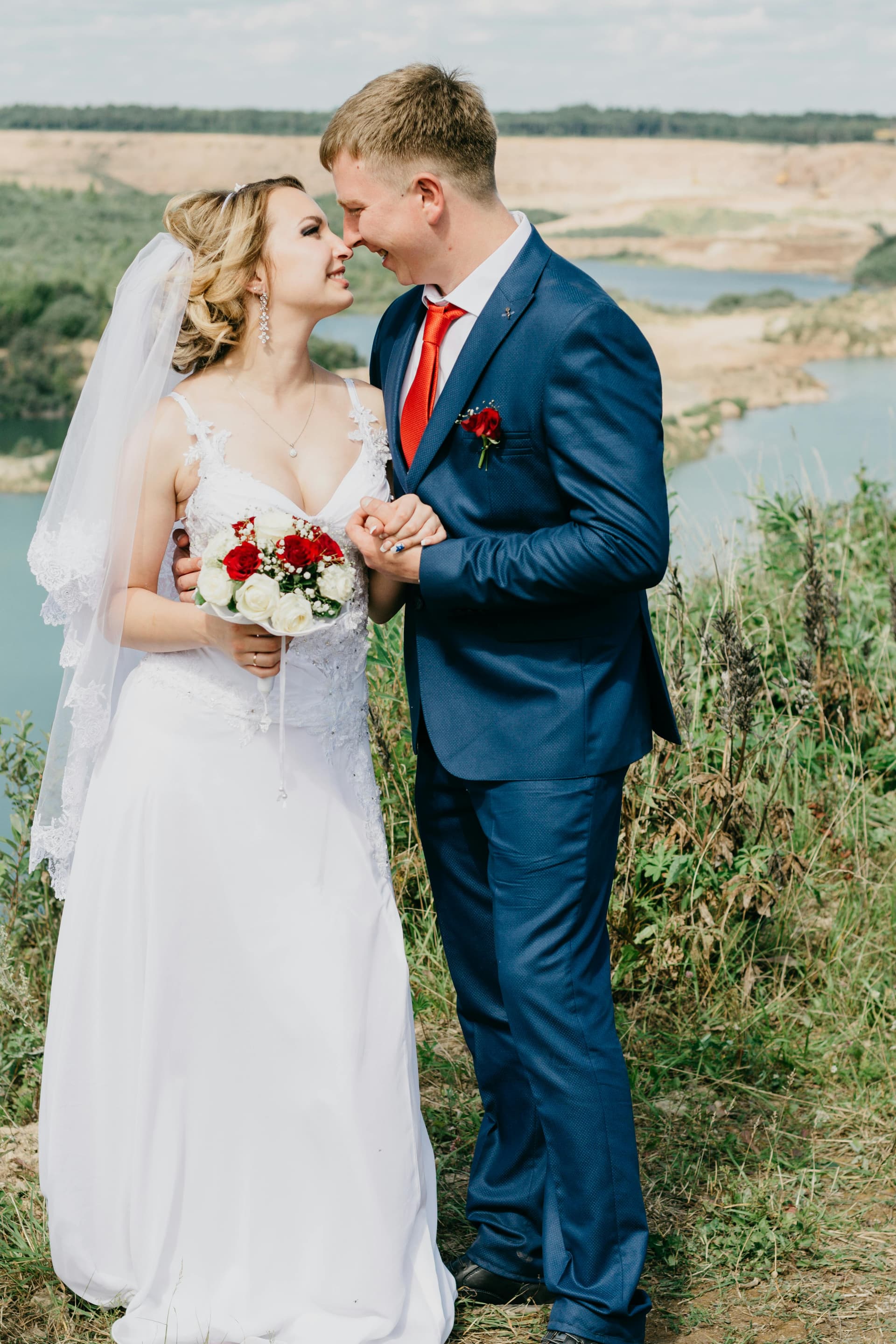 Wedding couple smiling with their foreheads touching and holding a white rose bouquet.